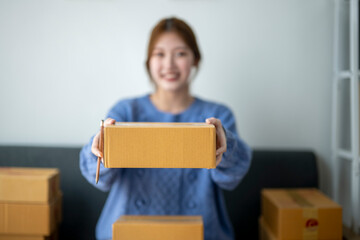 A woman is holding a cardboard box and smiling. The box is brown and he is a package
