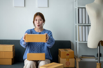 A woman is sitting on a couch with a box in her hand. She is wearing a blue sweater and has a...