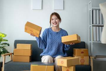 A woman is sitting on a couch with a pile of boxes in front of her. She is holding up two boxes and...