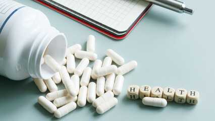 Medicine or vitamins - white medical capsules next to an open container, a notepad, a fountain pen...