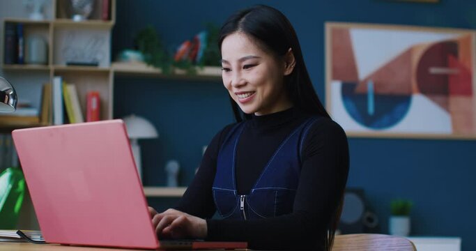 Charming Chinese girl sitting at desk. Working remotely or studying. Student typing messages on keyboard. Concept of remote communication. Browsing web or social media. Online chat.
