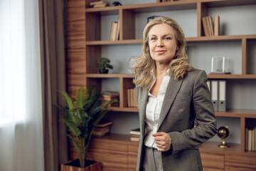 Woman psychotherapist in gray suit posing at her workplace in office