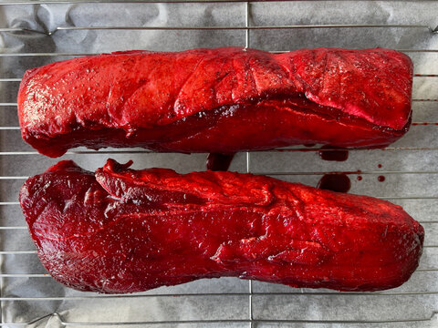 Two pieces of raw pork sirloin meat marinated in Chinese style red cha siu bbq sauce on an oven rack ready to roast