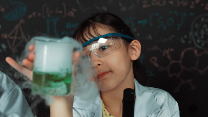 Young girl holding green chemical solution and inspect carefully while sitting in front of...