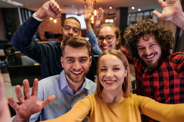 A diverse group of business professionals take a break from their tasks in a modern startup office to capture a creative selfie, showcasing teamwork and a vibrant workplace culture