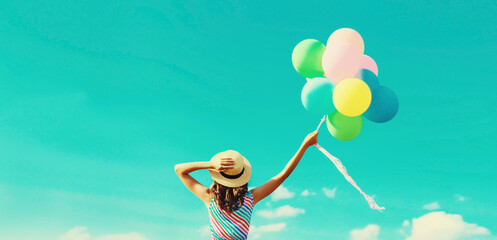 Happy joyful woman with bunch of colorful balloons in summer straw hat on blue sky background - Powered by Adobe