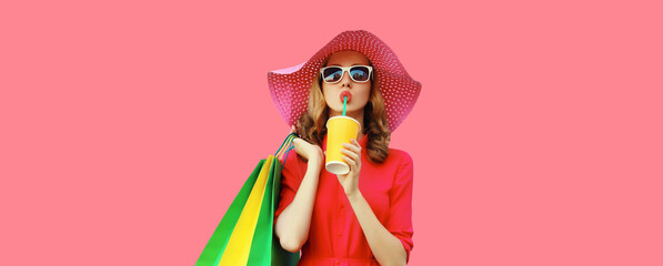 Portrait of beautiful young woman model with colorful shopping bags drinking juice in summer hat