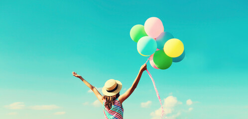 Happy joyful woman with bunch of colorful balloons in summer straw hat on blue sky background
