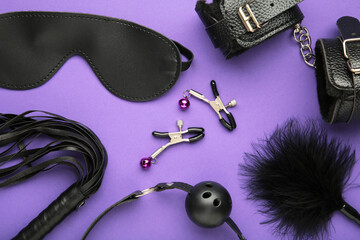 Set of erotic toys for BDSM on violet background. The game of sexual slavery with a whip, gag and leather blindfold. Intimate sex games. Space for text