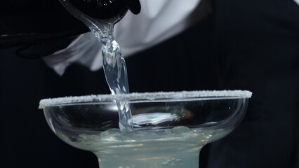 Professional bartender pouring fresh margarita with salted garnish glass. Macrography of skilled...