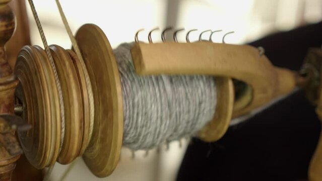 Closeup: Bobbin of grey wool yarn spins on vintage spinning wheel