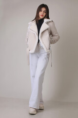Portrait of a beautiful fashion model in the studio on a light background, wearing a winter clothes and white trousers