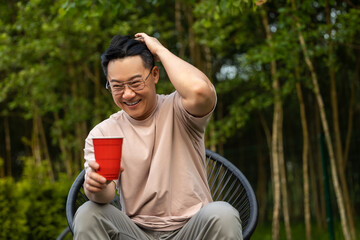 Man sitting on nature with beverage expressing cheerful expression during picnic