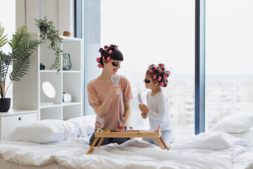 Cheerful mother and daughter singing using combs as microphones during beauty treatments at home on...