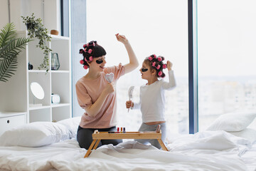 Caucasian young woman and little girl curling hair and applying eye patches. Cheerful mother and...