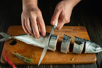 The chef hands cut the mackerel into pieces with a knife before frying it for dinner. Working...