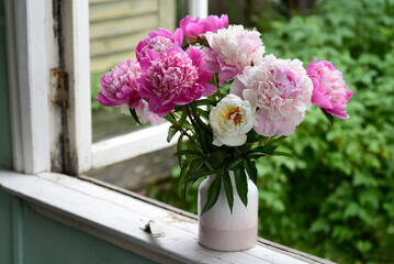 A bouquet of pink peonies in a vase on the windowsill of an old country home, a summer cottage.