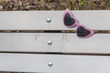 
pink children's sunglasses in the shape of a heart placed on a wooden bench