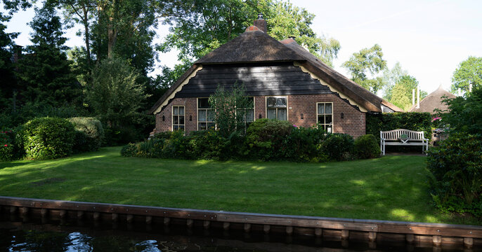 Typical houses of Giethoorn, Netherlands with gardens. Town is know as "Venice of the North". Landscaped view of the famous village with canals and rustic thatched roofs in the farm area.