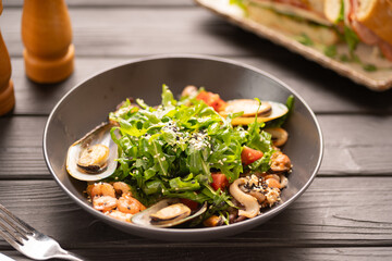 Seafood salad with shrimp, mussels, squid and arugula served on a plate on a wooden table