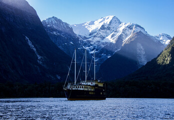 Boat on Milford Sound Fiordland New Zealand surrounded by snow clapped mountains with sun rays...