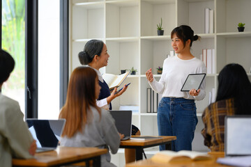 Asian college student presenting project on digital tablet to classmates and teacher during class