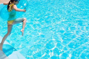 A little girl with an inflatable circle jumped into the pool. A cute kid in a swimsuit
