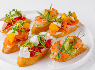 Elegant platter of assorted bruschetta with fresh toppings on a white background