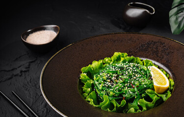 Fresh green seaweed salad with sesame seeds on dark plate