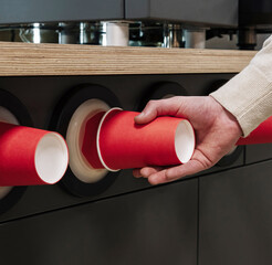 Person grabbing disposable red cup from dispenser