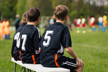Soccer Academy Youth Team. Three Football Boys on Substitute Bench Players Watching the Game and Ready To Play the Game. Kids in Black Soccer Jerseys Play the Junior Soccer League Competition