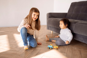 Little girls of different races sit and play in the living room of the house. Cute different...