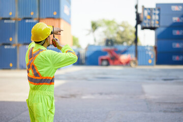 back view worker or engineer using walkie talkie and showing gesture to crane car in containers...