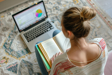 view from top as young woman learning language by reading a few books, while sitting on the floor, during online courses, laptop with lessons on the background