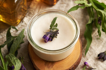 A jar of homemade comfrey root cream with fresh blooming knitbone plant