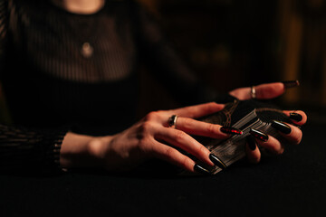 Closeup hands of unrecognizable female fortune-teller shuffling deck of tarot cards by light of...