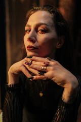Closeup face of fortune teller with black nails sitting at table in dark esoteric room with...