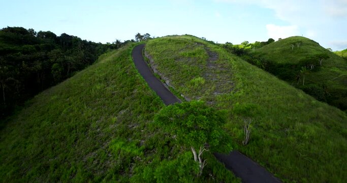 Woman rides scooter up lush Teletubbies Hills, Nusa Penida, Indonesia. Aerial