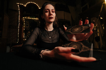 Low-angle portrait of fortuneteller shuffling deck of tarot cards by light of burning candles,...