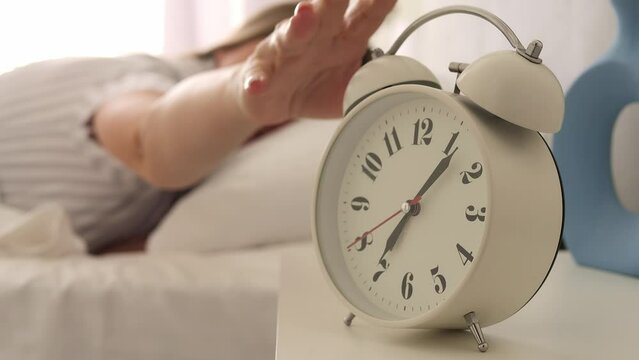 The woman reaches for the alarm clock, drowning out its insistent hum. The room fills with relentless rhythm of the alarm clock as she tries to turn it off, alarm clock starting her daily routine.