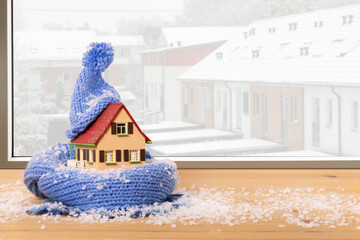 snow-covered model house with hat and scarf on a window sill in front of a row of snow-covered...