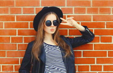 stylish young woman model wearing black round hat, leather jacket in rock style on city street