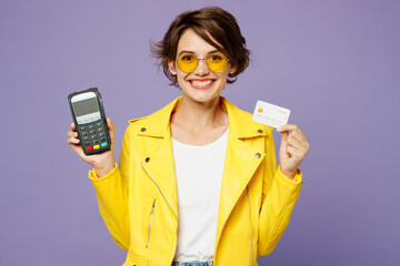 Young woman she wear yellow shirt white t-shirt casual clothes glasses hold wireless modern bank payment terminal to process acquire credit card isolated on plain purple background. Lifestyle concept