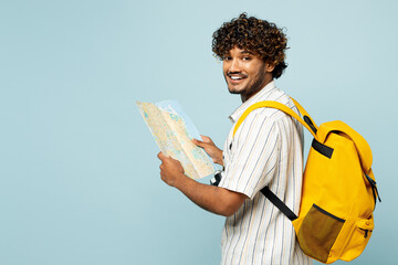 Sideways traveler Indian man wear white casual clothes backpack hold read map isolated on plain...