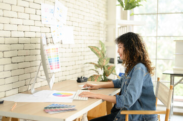 Young female graphic designers sitting at desks working with computer graphics color charts and...