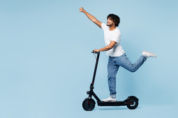 Full body young happy Indian man he wear white t-shirt casual clothes ride electric scooter do flying super hero gesture isolated on plain pastel light blue cyan background studio. Lifestyle concept. © ViDi Studio