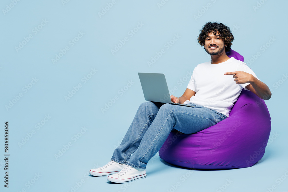 Sticker full body young happy indian man wear white t-shirt casual clothes sit in bag chair hold use work po