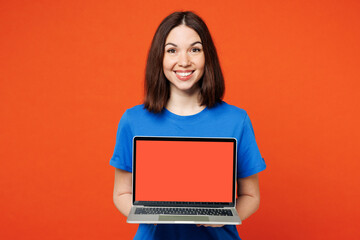 Naklejka premium Young smiling happy IT woman she wear blue t-shirt casual clothes hold use work on laptop pc computer with blank screen workspace area isolated on plain red orange background studio Lifestyle concept