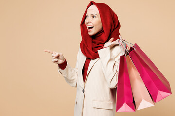 Young Arabian Muslim woman wear red abaya hijab suit clothes shopping hold package bag point finger...