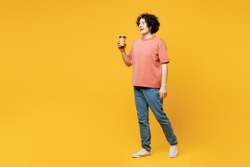Full body young happy man he wear pink t-shirt casual clothes hold takeaway delivery craft paper brown cup coffee to go isolated on plain yellow orange background studio portrait. Lifestyle concept.